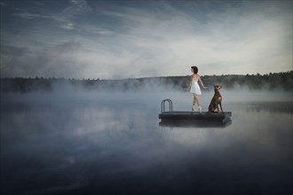 Caucasian ballet dancer on floating dock in foggy lake with dog