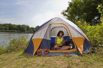 Hispanic woman using digital tablet in camping tent at lake