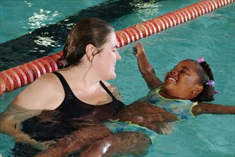 Woman teaching girl to swim in swimming pool