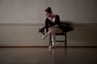 Caucasian ballerina sitting on chair tying ballet shoes