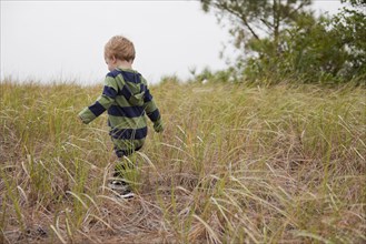 Caucasian boy walking in field of tall grass