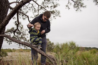 Caucasian father helping son walk on tree branch
