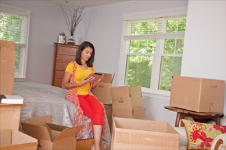 Hispanic woman using digital tablet in bedroom with cardboard boxes