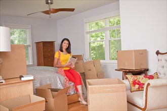 Smiling Hispanic woman using digital tablet in bedroom with cardboard boxes