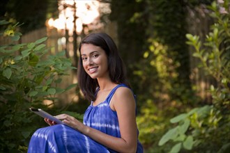Smiling Hispanic woman using digital tablet in backyard