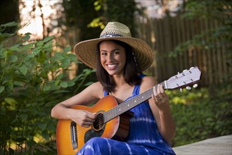 Smiling Hispanic woman playing guitar on patio in backyard