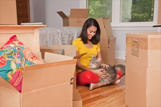 Hispanic woman sitting on floor petting cat near moving boxes