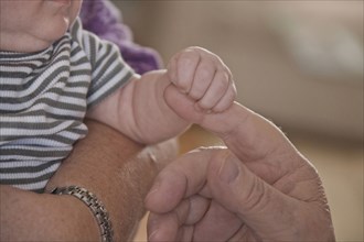 Caucasian baby boy holding finger of grandfather