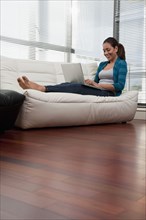 Hispanic woman on sofa using laptop