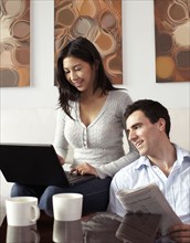 Couple relaxing together with newspaper and laptop