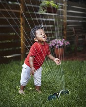 African American baby playing in sprinkler
