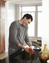 Man washing carrots and talking on telephone