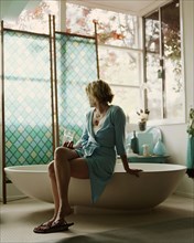 Woman sitting on edge of bathtub
