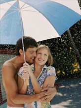 Caucasian couple hugging under umbrella