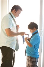 Hispanic father showing son how to tie necktie