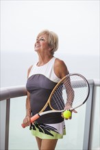Older Caucasian woman holding tennis racket on balcony