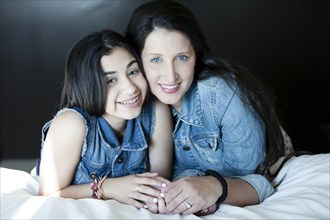 Hispanic mother and daughter smiling on bed