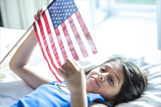 Hispanic girl holding American flag on bed