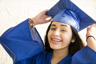 Smiling Hispanic girl wearing graduation robe and mortarboard