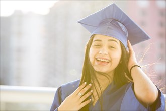 Smiling Hispanic girl wearing graduation robe and mortarboard