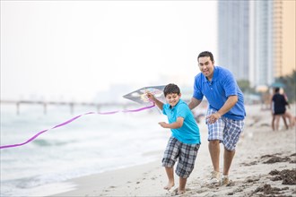 Hispanic father and son flying kite on beach
