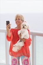 Older Caucasian woman taking selfie with dog on balcony
