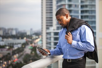 African American businessman using cell phone on urban balcony
