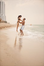 Man lifting girlfriend in ocean waves on beach