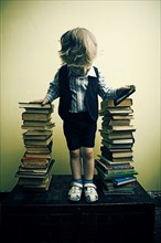 Boy holding cell phone near stacks of books