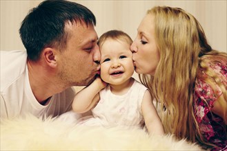 Caucasian parents kissing baby daughter in bed