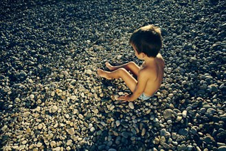 High angle view of boy sitting on rocky beach