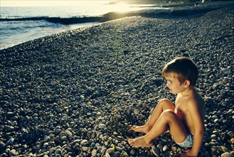 High angle view of boy sitting on rocky beach