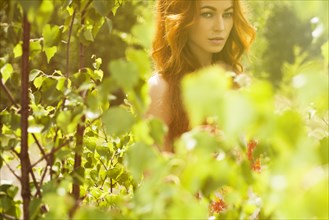 Caucasian woman posing behind foliage