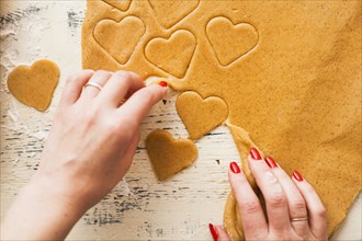 Hands of woman separating heart shapes cut from cookie dough