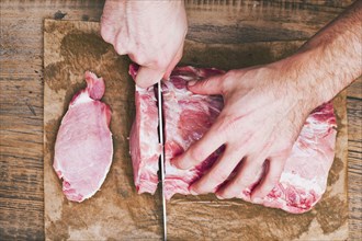 Hands of man cutting raw meat on butcher paper with knife