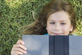 Smiling girl laying on ground reading book