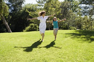 Mother and daughter running down hill in park