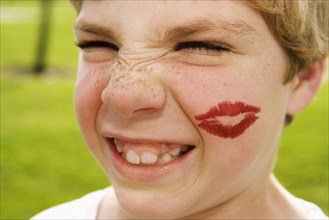 Grimacing boy with lipstick kiss on face
