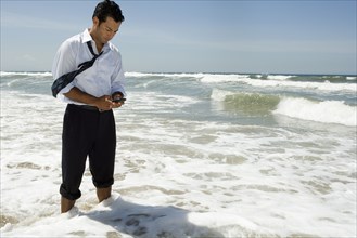 Businessman text messaging on cell phone while standing in ocean