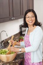 Chinese woman tossing salad in kitchen