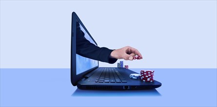 Hand holding gambling chips emerging from laptop screen