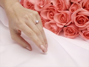Hand of woman wearing engagement ring near roses