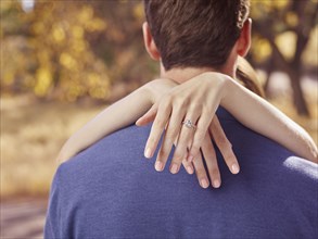 Hands of woman wearing engagement ring hugging man