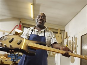 Black craftsman holding electric guitar in workshop