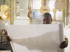 Black craftsman in guitar workshop looking at blueprints