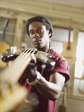 African American craftsman looking at guitar in workshop