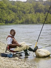 Black man with cell phone fishing in stream
