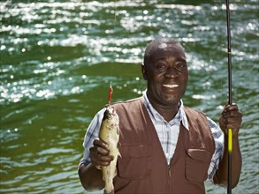 Black man holding fish and fishing rod near stream