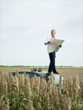 Caucasian businessman on top of car in field looking at map