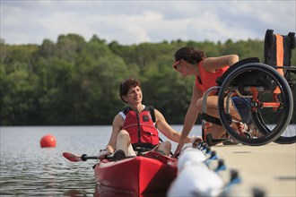 Caucasian instructor helping paraplegic woman with kayak